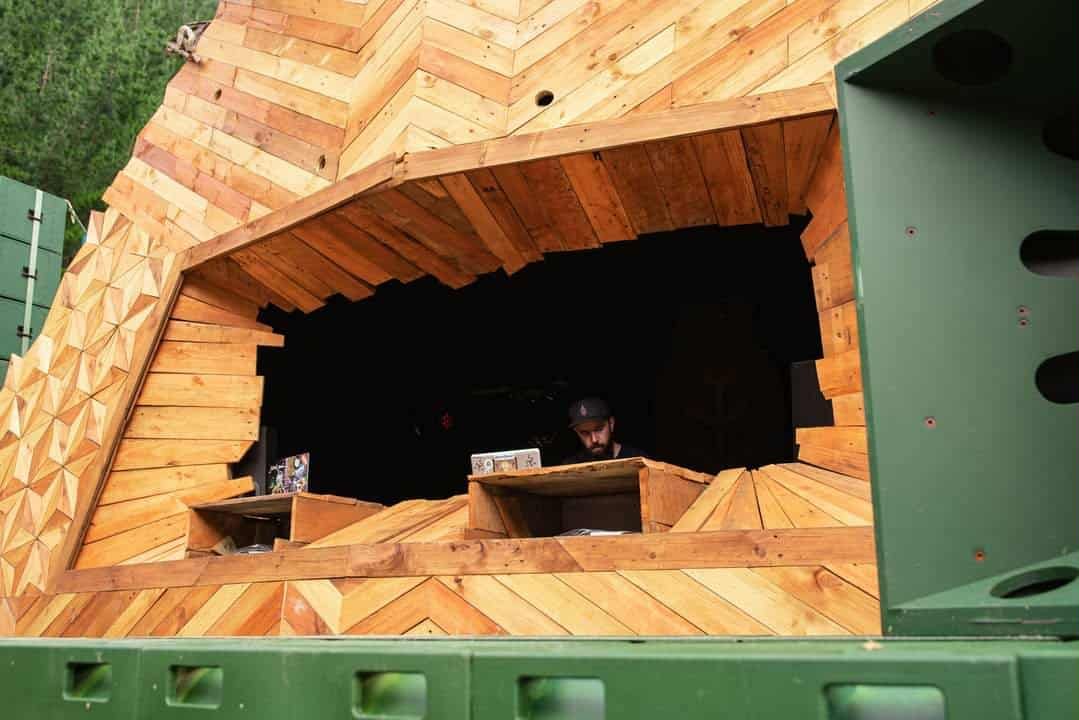 A DJ booth window embedded in a detailed wooden panel, built so there is depth and texture at every point